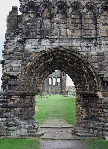 Атмосферный пейзаж аббатства Сент-Эндрюс в Шотландии, рушащаяся готическая архитектура, окруженная призрачным кладбищем под пасмурным прибрежным небом.