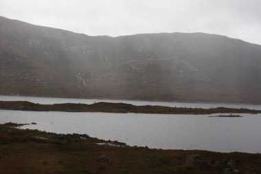 İskoçya 'da sonbaharda dağ zirveleri ve engebeli yamaçlarla çevrili bir dağ gölü. İskoçya' nın dramatik dağlık arazisini yansıtan bir su.
