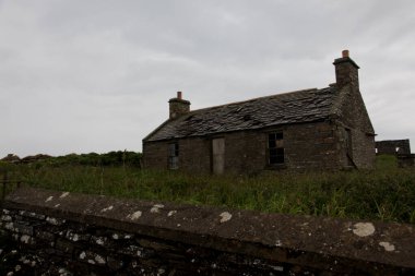 Vahşi İskoçya 'da terk edilmiş antik taş ev engebeli bozkırlar, yeşil tarlalar, sisli atmosfer manzarası ve İskoçya kırsalındaki dramatik bulutlu gökyüzü ile çevrili ıssız bir harabe bina.