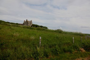 Vahşi İskoçya 'da terk edilmiş antik taş ev engebeli bozkırlar, yeşil tarlalar, sisli atmosfer manzarası ve İskoçya kırsalındaki dramatik bulutlu gökyüzü ile çevrili ıssız bir harabe bina.