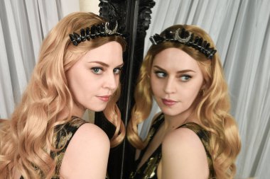 Şık siyah elbisesi olan, fantezi tacıyla sarışın bir kadının portresi. Süslü gotik aynaya bakıyor. Eskimiş desenli duvar kâğıdı arka planı..