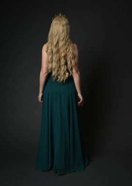 Kraliyet yeşil balo elbisesi giyen sarışın kadın modelin tam boy portresi, fantezi tacı. Durmak, uzaklaşmak, arka plan, karanlık stüdyo arka planında izole bir figür..