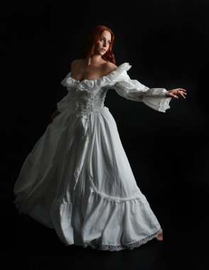 Tam boy portre güzel kadın model antika beyaz hayalet gelinlik giyiyor. Dalgalı kumaş elbiseyle dans pozu. Karanlık stüdyo arka planında izole bir figür.