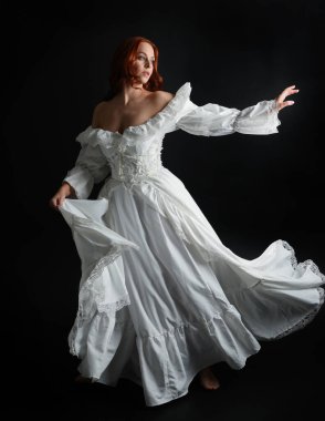 Tam boy portre güzel kadın model antika beyaz hayalet gelinlik giyiyor. Dalgalı kumaş elbiseyle dans pozu. Karanlık stüdyo arka planında izole bir figür.