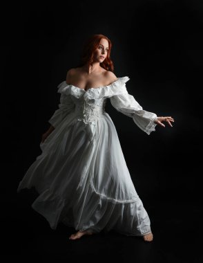 Tam boy portre güzel kadın model antika beyaz hayalet gelinlik giyiyor. Dalgalı kumaş elbiseyle dans pozu. Karanlık stüdyo arka planında izole bir figür.