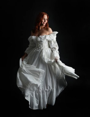 Tam boy portre güzel kadın model antika beyaz hayalet gelinlik giyiyor. Dalgalı kumaş elbiseyle dans pozu. Karanlık stüdyo arka planında izole bir figür.
