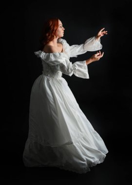 Tam boy portre güzel kadın model antika beyaz hayalet gelinlik giyiyor. Dalgalı kumaş elbiseyle dans pozu. Karanlık stüdyo arka planında izole bir figür.