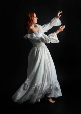 Tam boy portre güzel kadın model antika beyaz hayalet gelinlik giyiyor. Dalgalı kumaş elbiseyle dans pozu. Karanlık stüdyo arka planında izole bir figür.