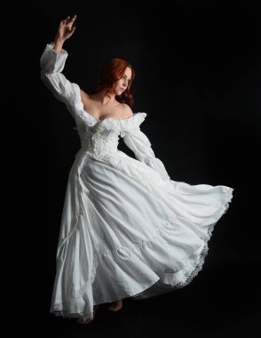 Tam boy portre güzel kadın model antika beyaz hayalet gelinlik giyiyor. Dalgalı kumaş elbiseyle dans pozu. Karanlık stüdyo arka planında izole bir figür.