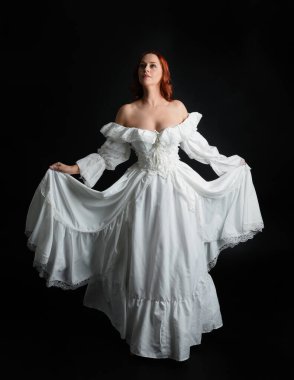 Tam boy portre güzel kadın model antika beyaz hayalet gelinlik giyiyor. Dalgalı kumaş elbiseyle dans pozu. Karanlık stüdyo arka planında izole bir figür.
