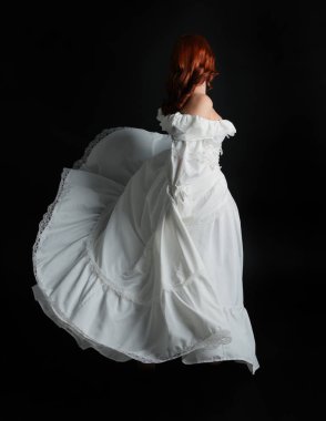 Tam boy portre güzel kadın model antika beyaz hayalet gelinlik giyiyor. Dans pozu, kameradan uzaklaşmak, arka plan. Karanlık stüdyo arka planında izole bir figür.