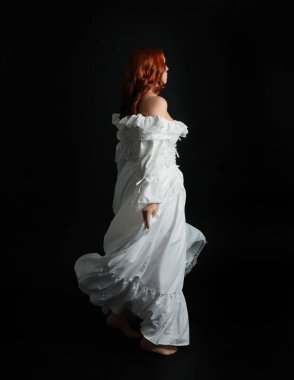 Tam boy portre güzel kadın model antika beyaz hayalet gelinlik giyiyor. Dans pozu, kameradan uzaklaşmak, arka plan. Karanlık stüdyo arka planında izole bir figür.