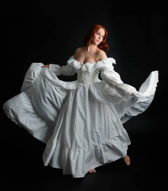 Tam boy portre güzel kadın model antika beyaz hayalet gelinlik giyiyor. Dalgalı kumaş elbiseyle dans pozu. Karanlık stüdyo arka planında izole bir figür.