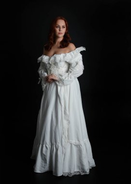 Tam boy portre güzel kadın model, kızıl saçlı, antika beyaz hayalet gelinlik giyiyor. Duruş, karanlık stüdyo arka planında izole bir figür