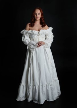 Tam boy portre güzel kadın model, kızıl saçlı, antika beyaz hayalet gelinlik giyiyor. Duruş, karanlık stüdyo arka planında izole bir figür