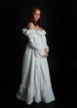 Tam boy portre güzel kadın model, kızıl saçlı, antika beyaz hayalet gelinlik giyiyor. Duruş, karanlık stüdyo arka planında izole bir figür