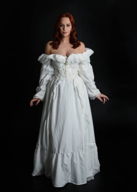 Tam boy portre güzel kadın model, kızıl saçlı, antika beyaz hayalet gelinlik giyiyor. Duruş, karanlık stüdyo arka planında izole bir figür