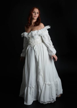 Tam boy portre güzel kadın model, kızıl saçlı, antika beyaz hayalet gelinlik giyiyor. Duruş, karanlık stüdyo arka planında izole bir figür