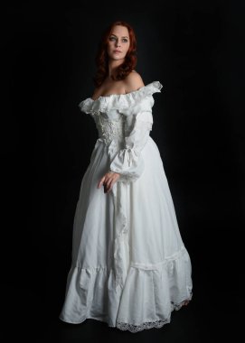 Tam boy portre güzel kadın model, kızıl saçlı, antika beyaz hayalet gelinlik giyiyor. Duruş, karanlık stüdyo arka planında izole bir figür