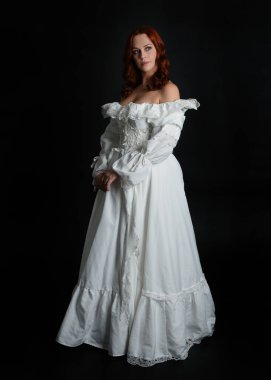 Tam boy portre güzel kadın model, kızıl saçlı, antika beyaz hayalet gelinlik giyiyor. Duruş, karanlık stüdyo arka planında izole bir figür