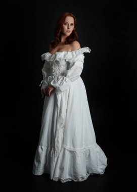 Tam boy portre güzel kadın model, kızıl saçlı, antika beyaz hayalet gelinlik giyiyor. Duruş, karanlık stüdyo arka planında izole bir figür