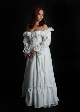 Tam boy portre güzel kadın model, kızıl saçlı, antika beyaz hayalet gelinlik giyiyor. Duruş, karanlık stüdyo arka planında izole bir figür