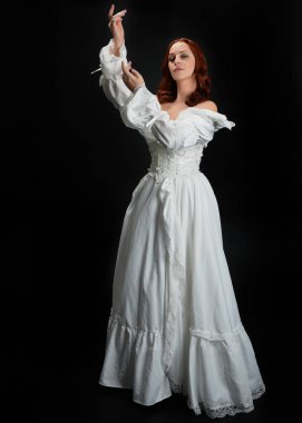 Tam boy portre güzel kadın model, kızıl saçlı, antika beyaz hayalet gelinlik giyiyor. Duruş, karanlık stüdyo arka planında izole bir figür