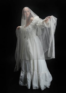 Tam boy portre güzel kadın model antika beyaz hayalet gelinlik gelinlik, ruhani duvak başörtüsü giyiyor. Karanlık stüdyo arka planında izole edilmiş bir şahsiyet.