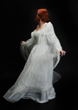 Tam boy portre güzel kadın model, kızıl saçlı, antika beyaz hayalet gelinlik giyiyor. Duruş arkası görünümü, karanlık stüdyo arka planında izole bir figür
