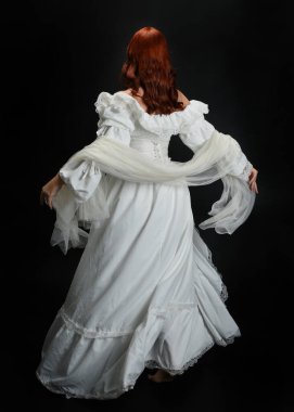 Tam boy portre güzel kadın model, kızıl saçlı, antika beyaz hayalet gelinlik giyiyor. Duruş arkası görünümü, karanlık stüdyo arka planında izole bir figür