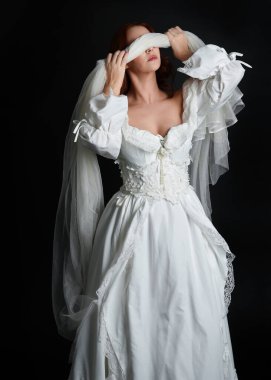 Kapalı portre güzel bayan model antika beyaz hayalet gelin gelinliği giyiyor peçeli bir maske takıyor. Karanlık stüdyo arka planında izole bir figür, el hareketleriyle.