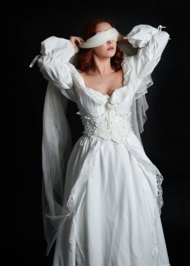 close up portrait beautiful female model wearing antique white historical ghost bride wedding dress gown, a veiled mask blindfold covering face. isolated figure on dark studio background, hands gesturing.
