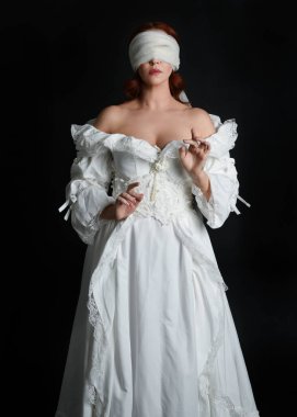 close up portrait beautiful female model wearing antique white historical ghost bride wedding dress gown, a veiled mask blindfold covering face. isolated figure on dark studio background, hands gesturing.