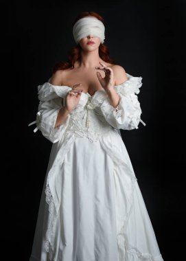 close up portrait beautiful female model wearing antique white historical ghost bride wedding dress gown, a veiled mask blindfold covering face. isolated figure on dark studio background, hands gesturing.