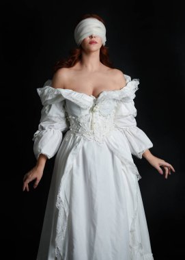 close up portrait beautiful female model wearing antique white historical ghost bride wedding dress gown, a veiled mask blindfold covering face. isolated figure on dark studio background, hands gesturing.