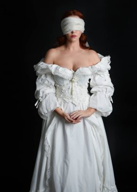 Kapalı portre güzel bayan model antika beyaz hayalet gelin gelinliği giyiyor peçeli bir maske takıyor. Karanlık stüdyo arka planında izole bir figür, el hareketleriyle.