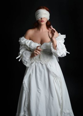 close up portrait beautiful female model wearing antique white historical ghost bride wedding dress gown, a veiled mask blindfold covering face. isolated figure on dark studio background, hands gesturing.