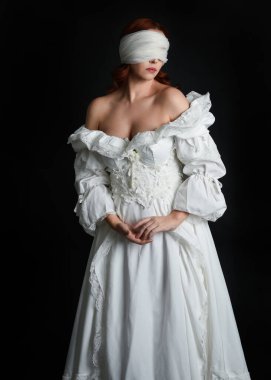 close up portrait beautiful female model wearing antique white historical ghost bride wedding dress gown, a veiled mask blindfold covering face. isolated figure on dark studio background, hands gesturing.