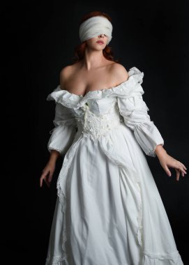 close up portrait beautiful female model wearing antique white historical ghost bride wedding dress gown, a veiled mask blindfold covering face. isolated figure on dark studio background, hands gesturing.