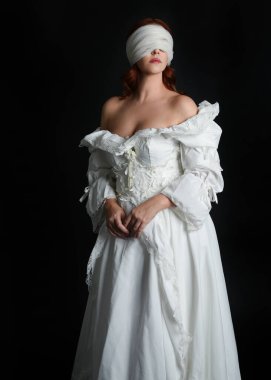 close up portrait beautiful female model wearing antique white historical ghost bride wedding dress gown, a veiled mask blindfold covering face. isolated figure on dark studio background, hands gesturing.