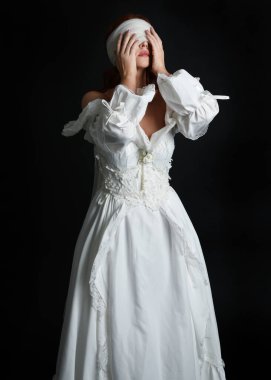 close up portrait beautiful female model wearing antique white historical ghost bride wedding dress gown, a veiled mask blindfold covering face. isolated figure on dark studio background, hands gesturing.