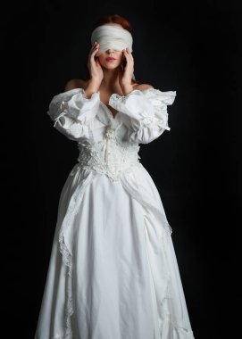 Kapalı portre güzel bayan model antika beyaz hayalet gelin gelinliği giyiyor peçeli bir maske takıyor. Karanlık stüdyo arka planında izole bir figür, el hareketleriyle.