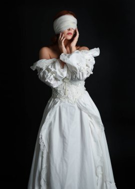 close up portrait beautiful female model wearing antique white historical ghost bride wedding dress gown, a veiled mask blindfold covering face. isolated figure on dark studio background, hands gesturing.