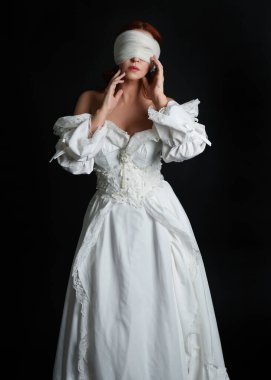 close up portrait beautiful female model wearing antique white historical ghost bride wedding dress gown, a veiled mask blindfold covering face. isolated figure on dark studio background, hands gesturing.