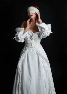 close up portrait beautiful female model wearing antique white historical ghost bride wedding dress gown, a veiled mask blindfold covering face. isolated figure on dark studio background, hands gesturing.