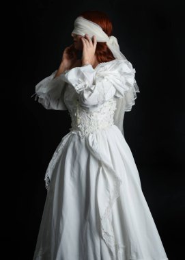 Kapalı portre güzel bayan model antika beyaz hayalet gelin gelinliği giyiyor peçeli bir maske takıyor. Karanlık stüdyo arka planında izole bir figür, el hareketleriyle.