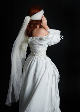 Kapalı portre güzel bayan model antika beyaz hayalet gelin gelinliği giyiyor peçeli bir maske takıyor. Karanlık stüdyo arka planında izole bir figür, el hareketleriyle.