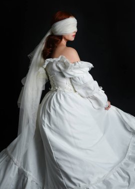 Kapalı portre güzel bayan model antika beyaz hayalet gelin gelinliği giyiyor peçeli bir maske takıyor. Karanlık stüdyo arka planında izole bir figür, el hareketleriyle.