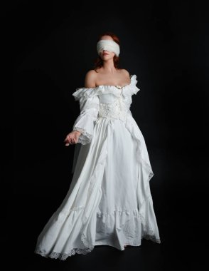 close up portrait beautiful female model wearing antique white historical ghost bride wedding dress gown, a veiled mask blindfold covering face. isolated figure on dark studio background, hand gesture