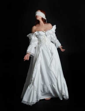 close up portrait beautiful female model wearing antique white historical ghost bride wedding dress gown, a veiled mask blindfold covering face. isolated figure on dark studio background, hand gesture